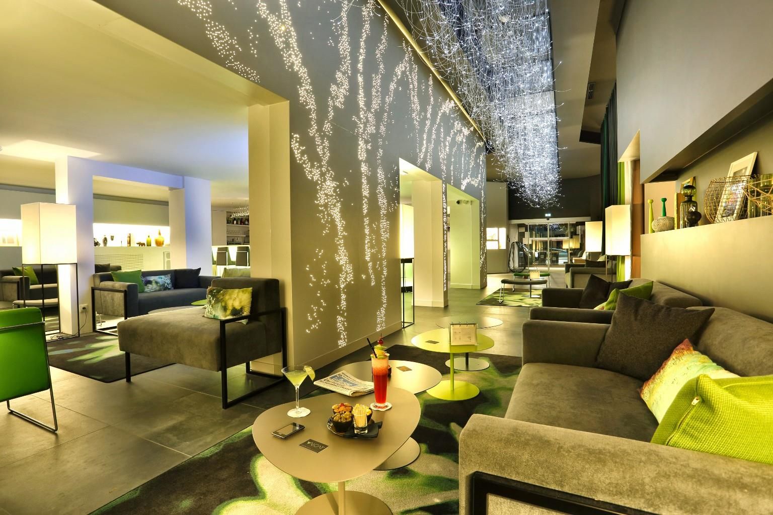 Un moderno vestíbulo de hotel con una zona de estar, un bar y una gran pared con una proyección de luz.