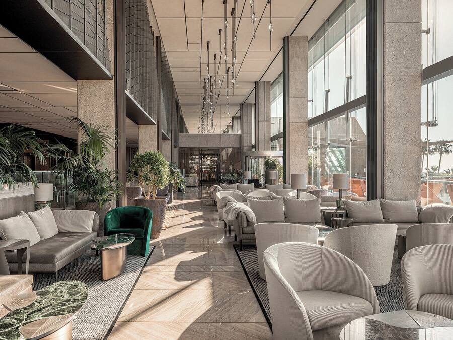 Un vestíbulo amplio con mobiliario moderno, ventanas grandes y plantas de interior.