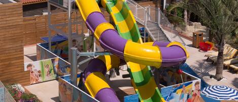 A water park with a large multi-colored water slide, a pool, and a view of the ocean.