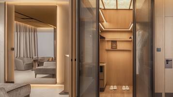 Une chambre d’hôtel moderne dotée d’une paroi en verre, d’un coin salon avec des canapés, d’une petite table et d’un porte-chaussures.