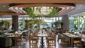 Un restaurante espacioso con una larga mesa dispuesta para comer, rodeado de asientos cómodos y grandes ventanales con vistas al exterior.