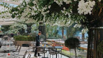 An outdoor dining area with tables and chairs, a waiter, and a view of the sea.