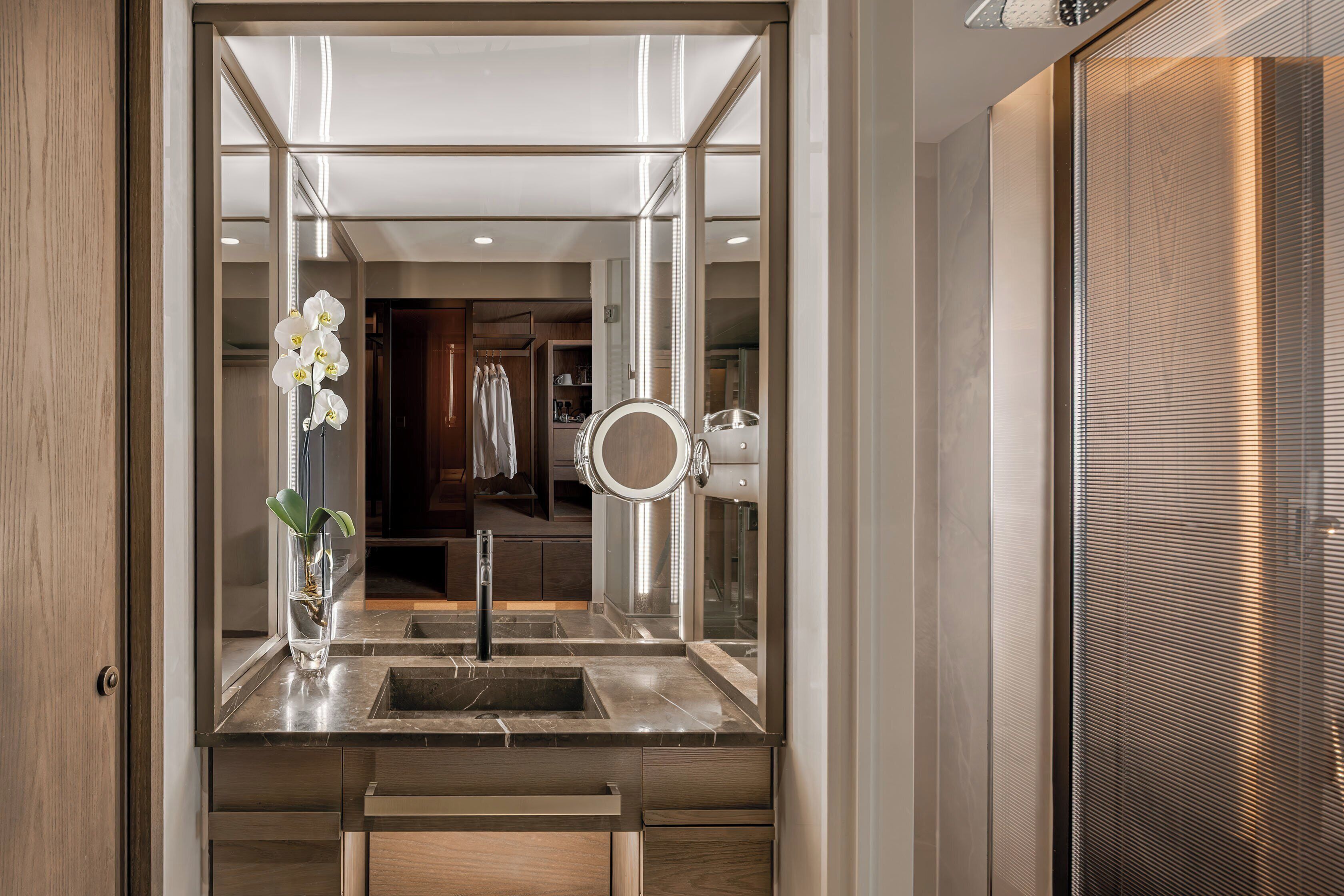 Un baño moderno con un espejo grande, un lavamanos y una orquídea en maceta.