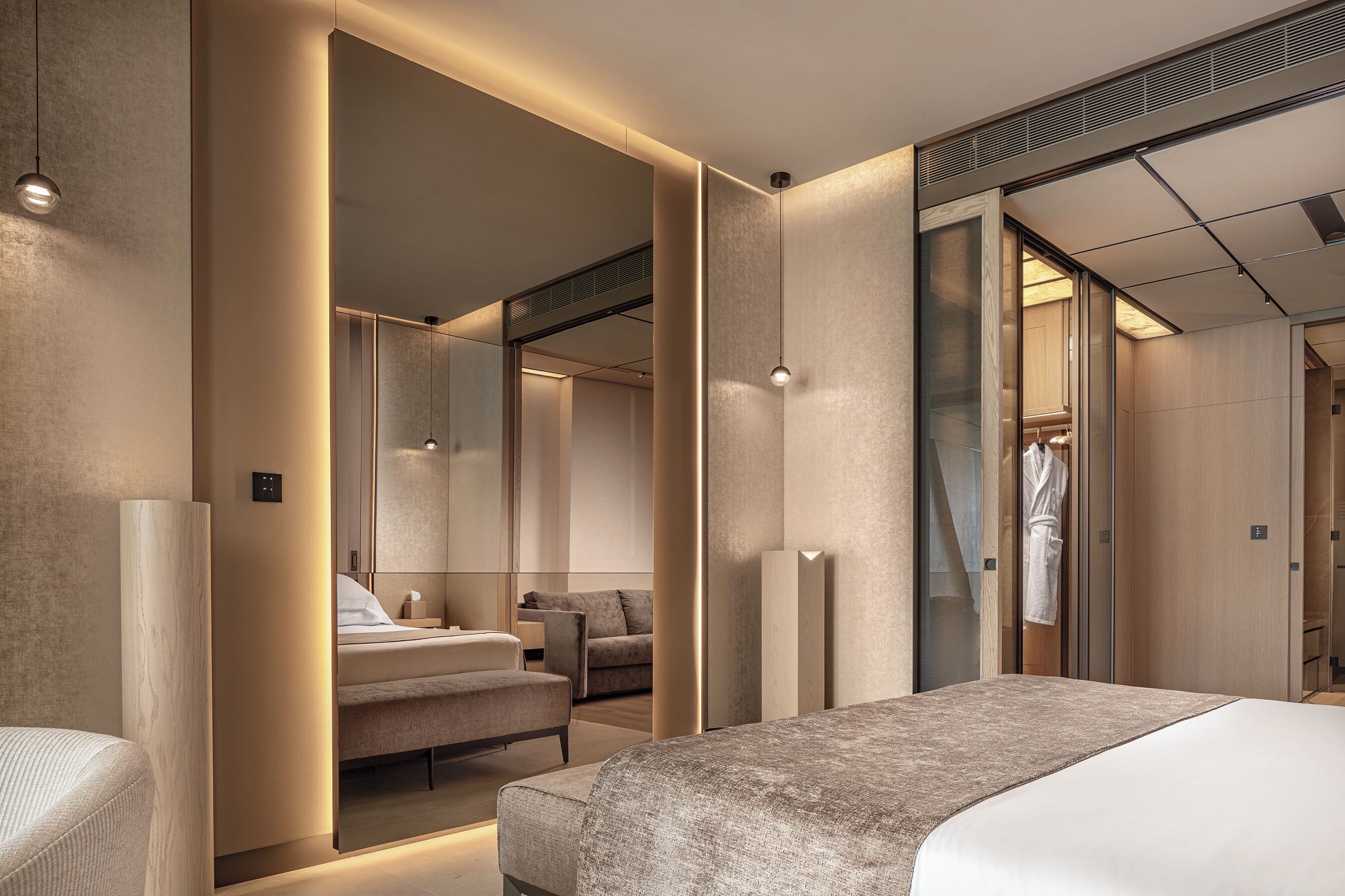 Habitación de hotel moderna con una cama grande, un espacio de descanso, un espejo y un vestidor.