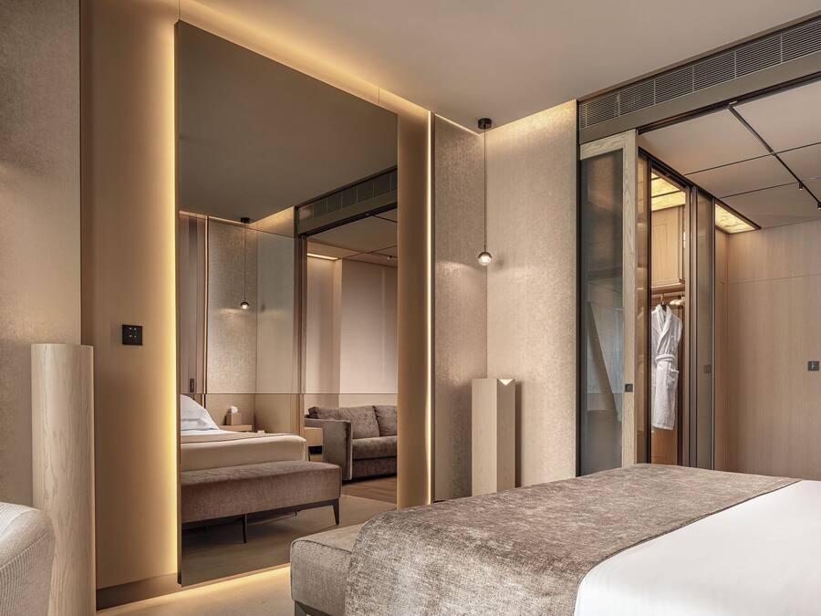 Habitación de hotel moderna con una cama grande, un espacio de descanso, un espejo y un vestidor.