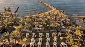 Un resort con vista a la playa, palmeras y tumbonas.