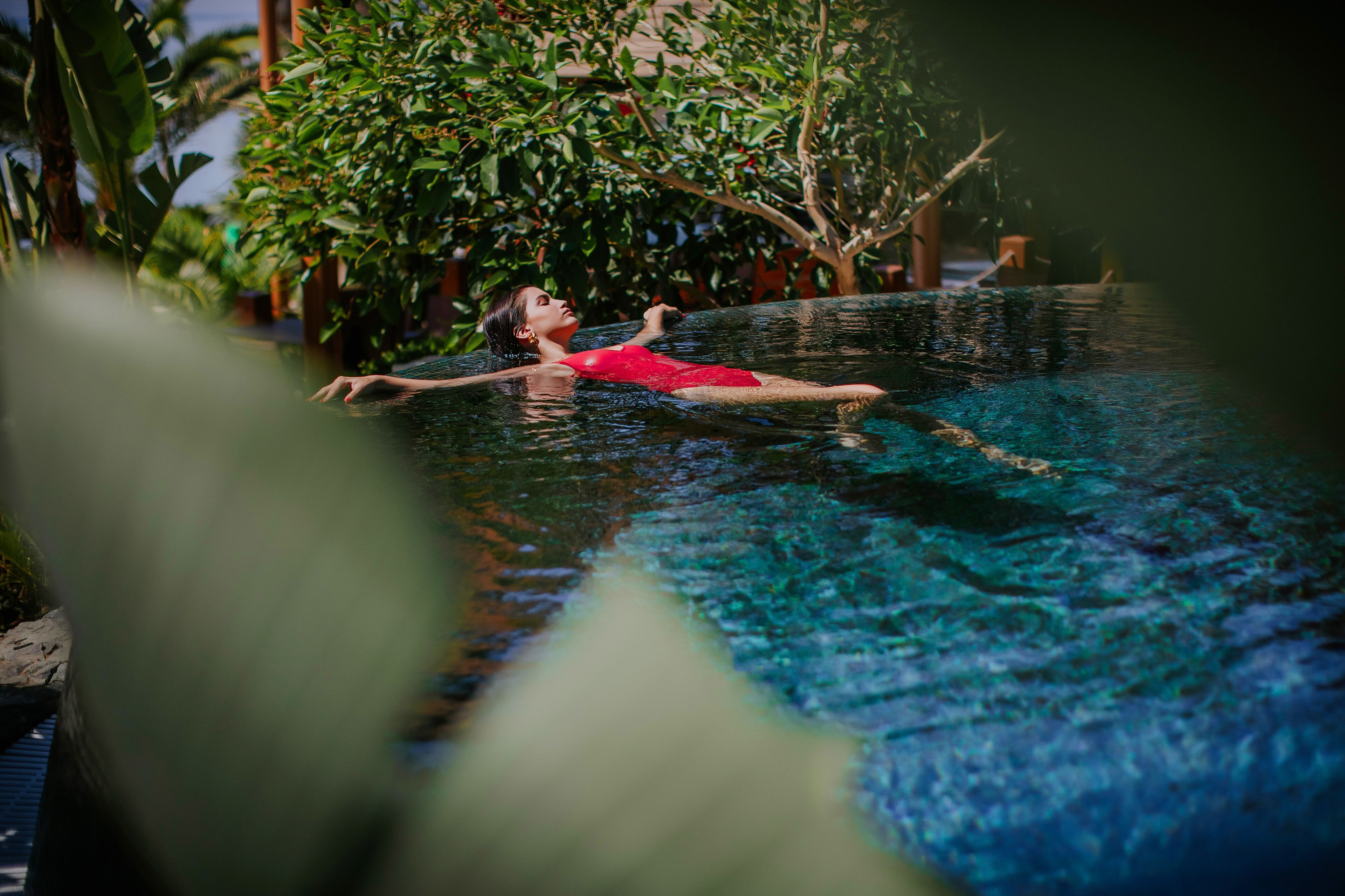 Eine Person im roten Badeanzug treibt in einem klaren Pool, im Hintergrund ein tropischer Garten.