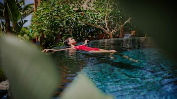 Una persona en traje de baño rojo flotando en una piscina cristalina con un jardín tropical al fondo.