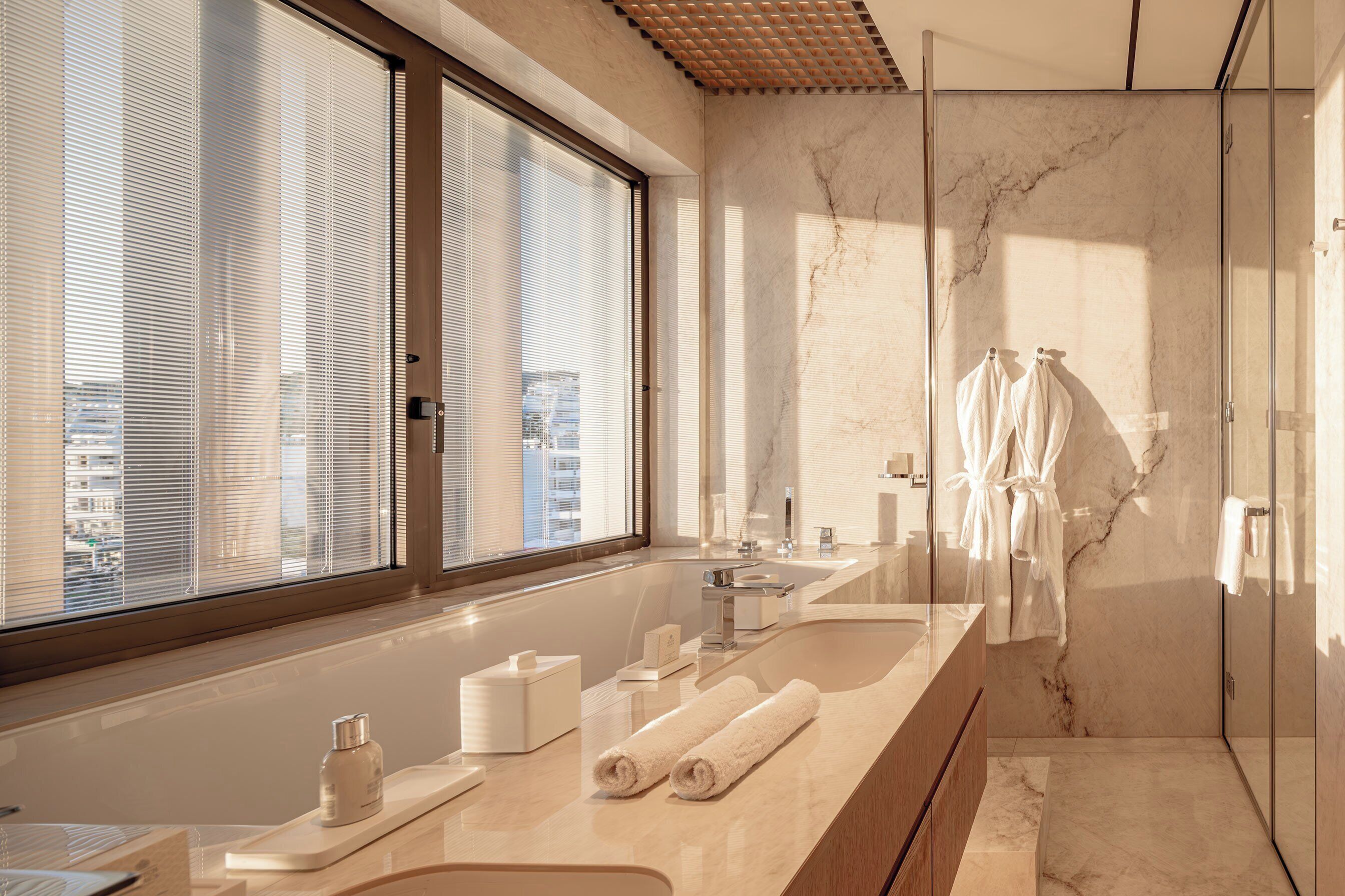 A modern bathroom with a large window, a marble sink, and a glass shower enclosure.