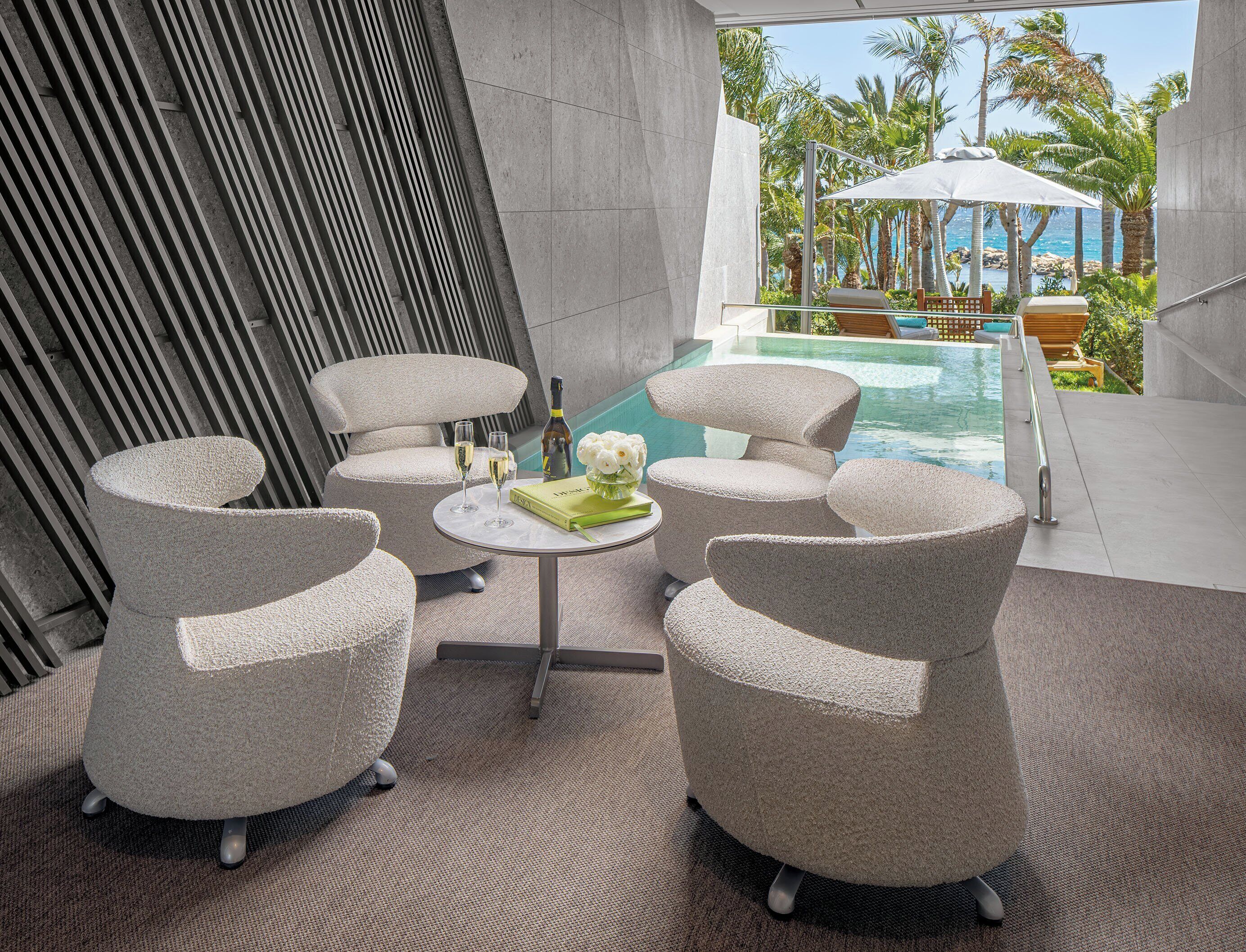 A modern outdoor seating area with a pool view, featuring lounge chairs and a table with drinks and a book.