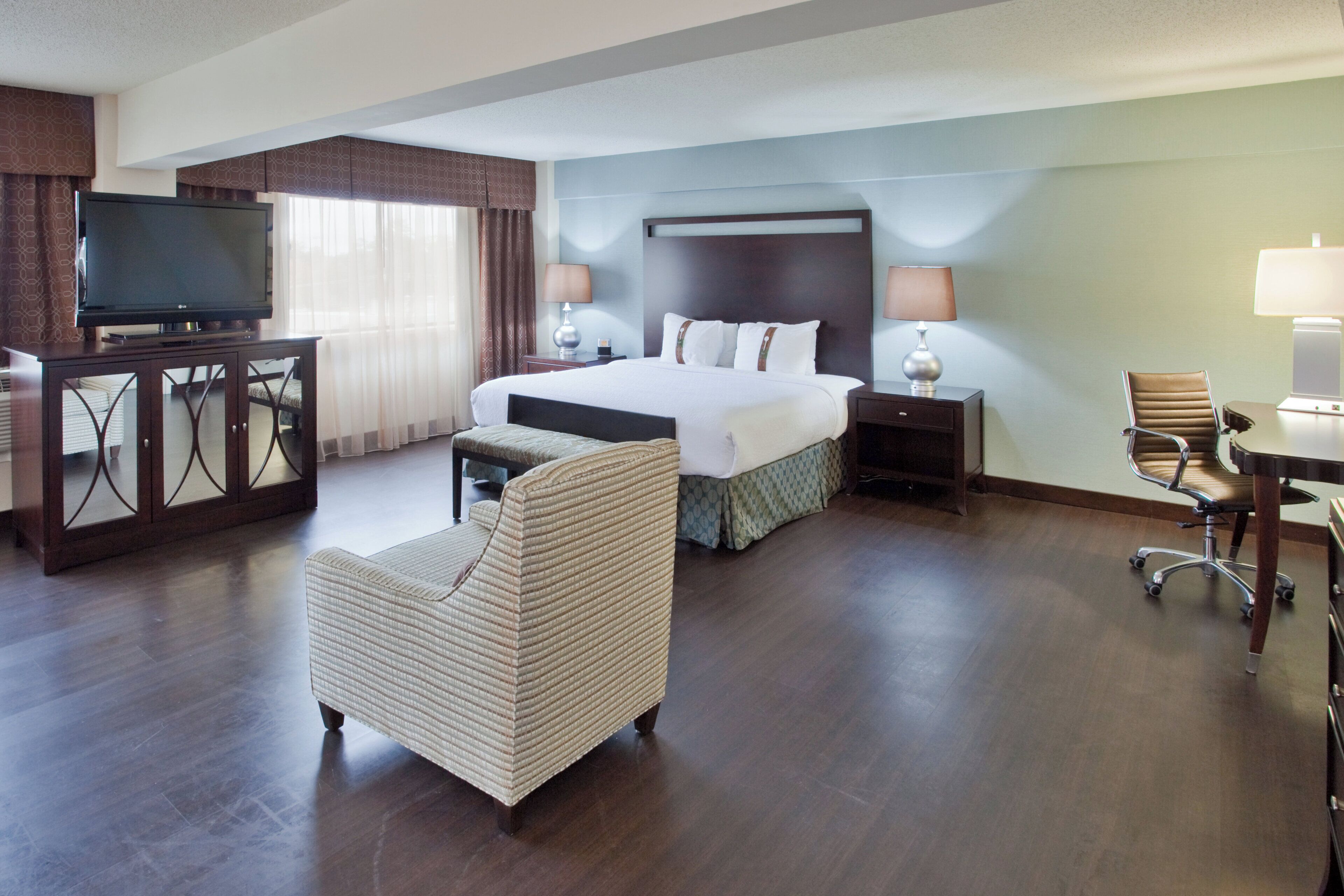 A hotel room with a bed, a television, a desk, a chair, and a lamp.