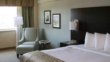 A hotel room with a bed, a chair, a small table, a lamp, and two framed pictures on the wall.