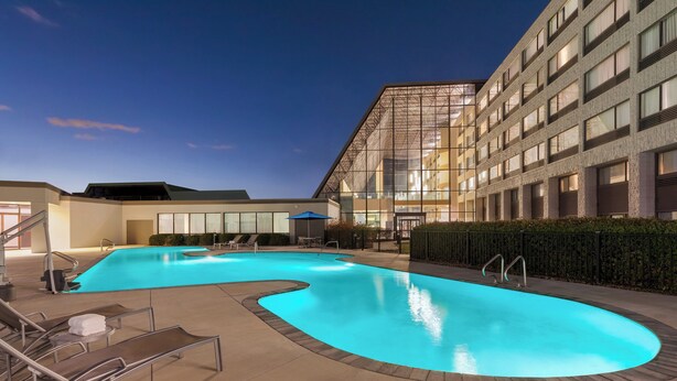 Piscina com espreguiçadeiras e um edifício com grandes janelas ao fundo.