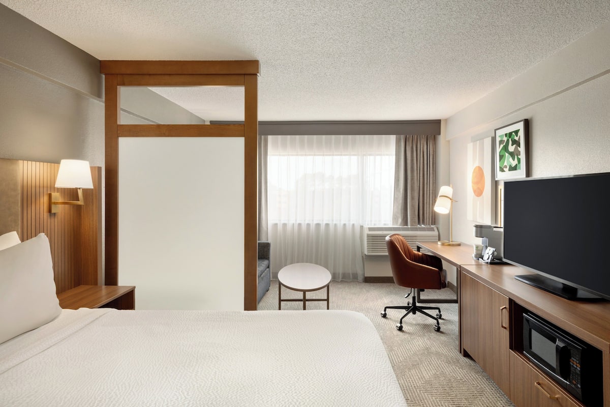 A hotel room with a bed, a desk, a television, and a window with curtains.