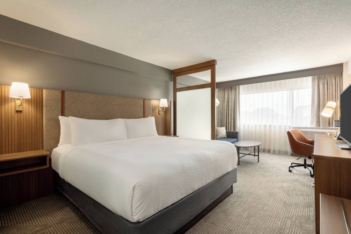 A hotel room with a large bed, a desk, a chair, and a mirror.