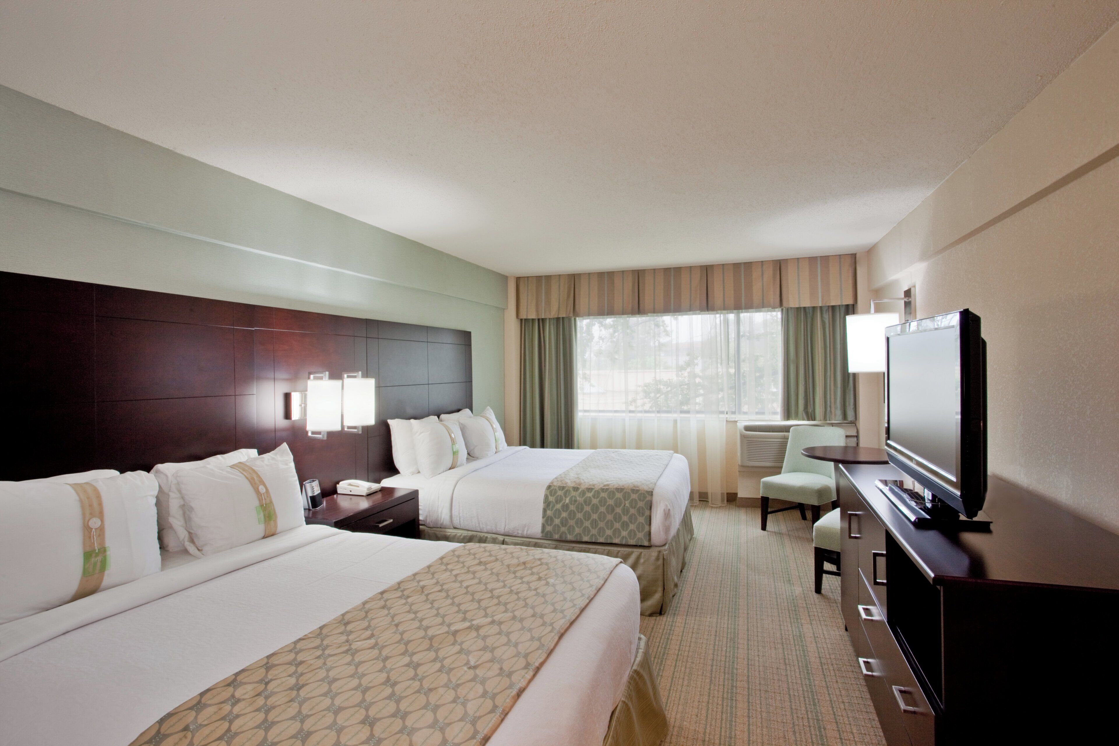 A hotel room with two beds, a television, a desk, and a chair.