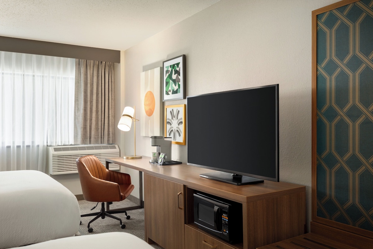 Ein Hotelzimmer mit Bett, Schreibtisch, Flachbildfernseher, Mikrowelle, Stuhl und Lampe.