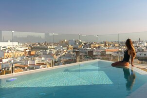 Una mujer sentada junto a una piscina con vistas a la ciudad.