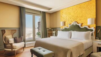 Une chambre d’hôtel avec un grand lit, une chaise longue, un banc, une table de chevet et une vue sur l’extérieur.