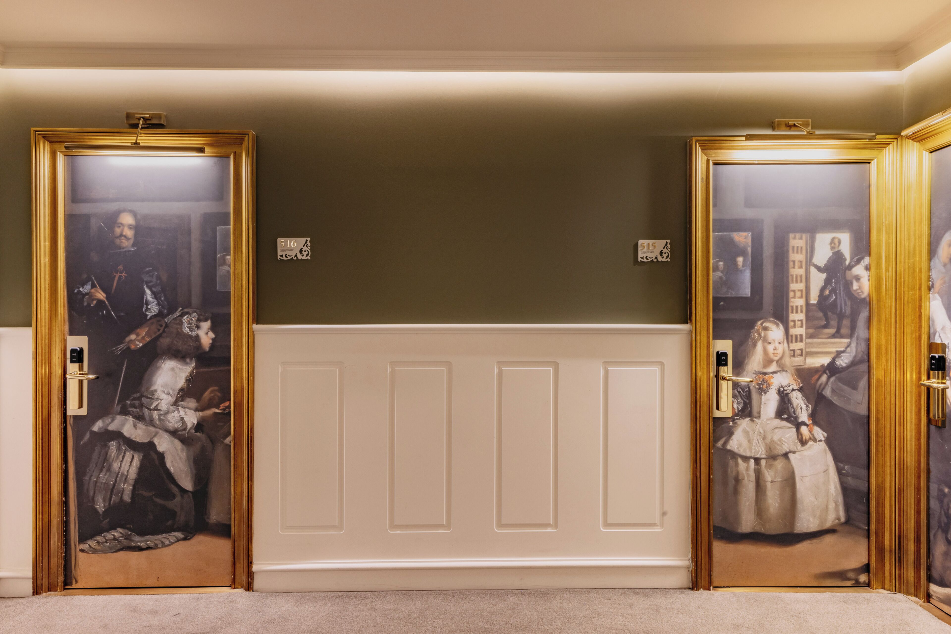 Un pasillo con dos puertas, cada una enmarcada en dorado, que dan a habitaciones con grandes cuadros enmarcados.