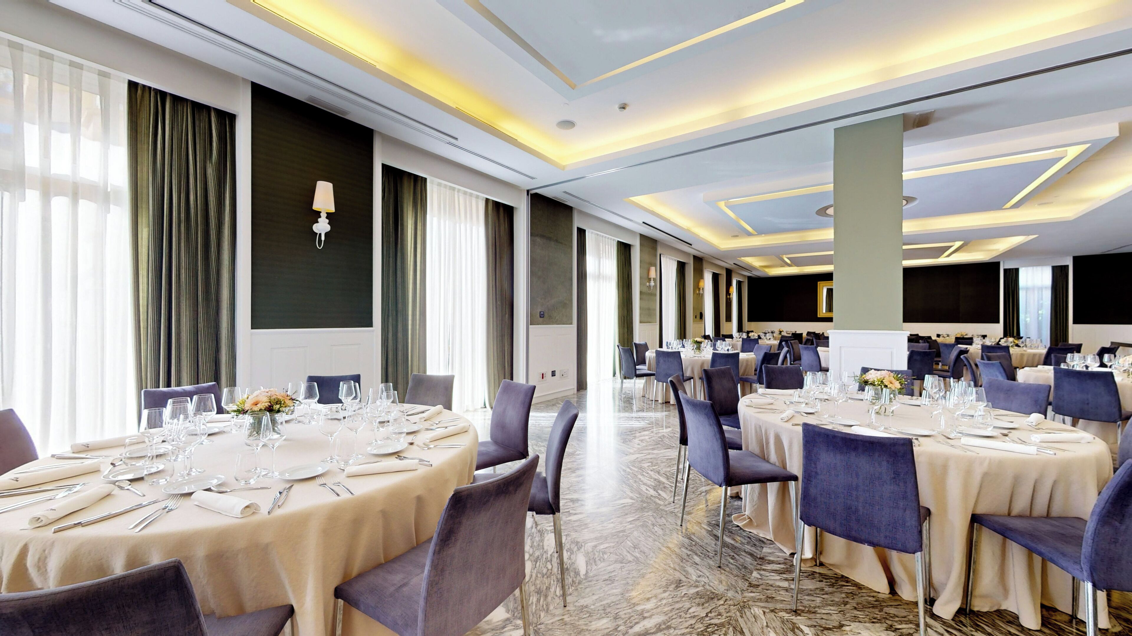Un amplio salón de banquetes con mesas redondas dispuestas para comer, con suelo de mármol e iluminación moderna.