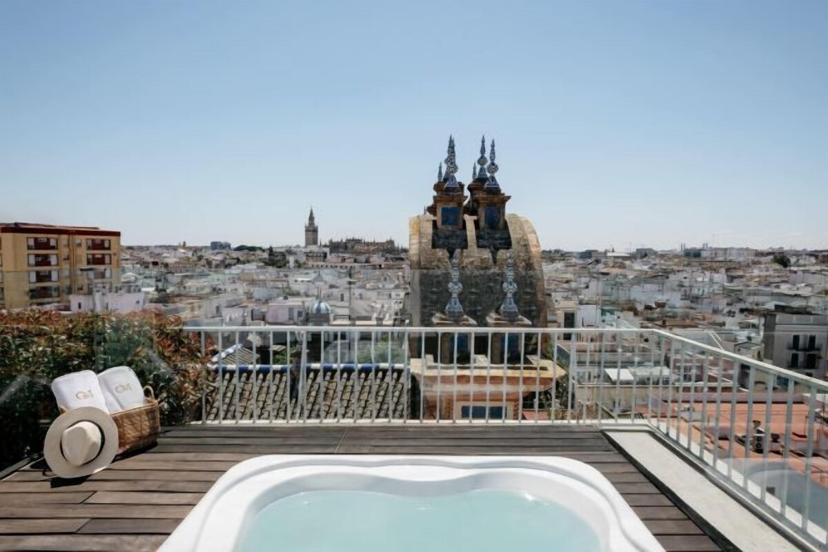 A rooftop terrace with a hot tub, a view of a cityscape, and a building with two spires in the background.