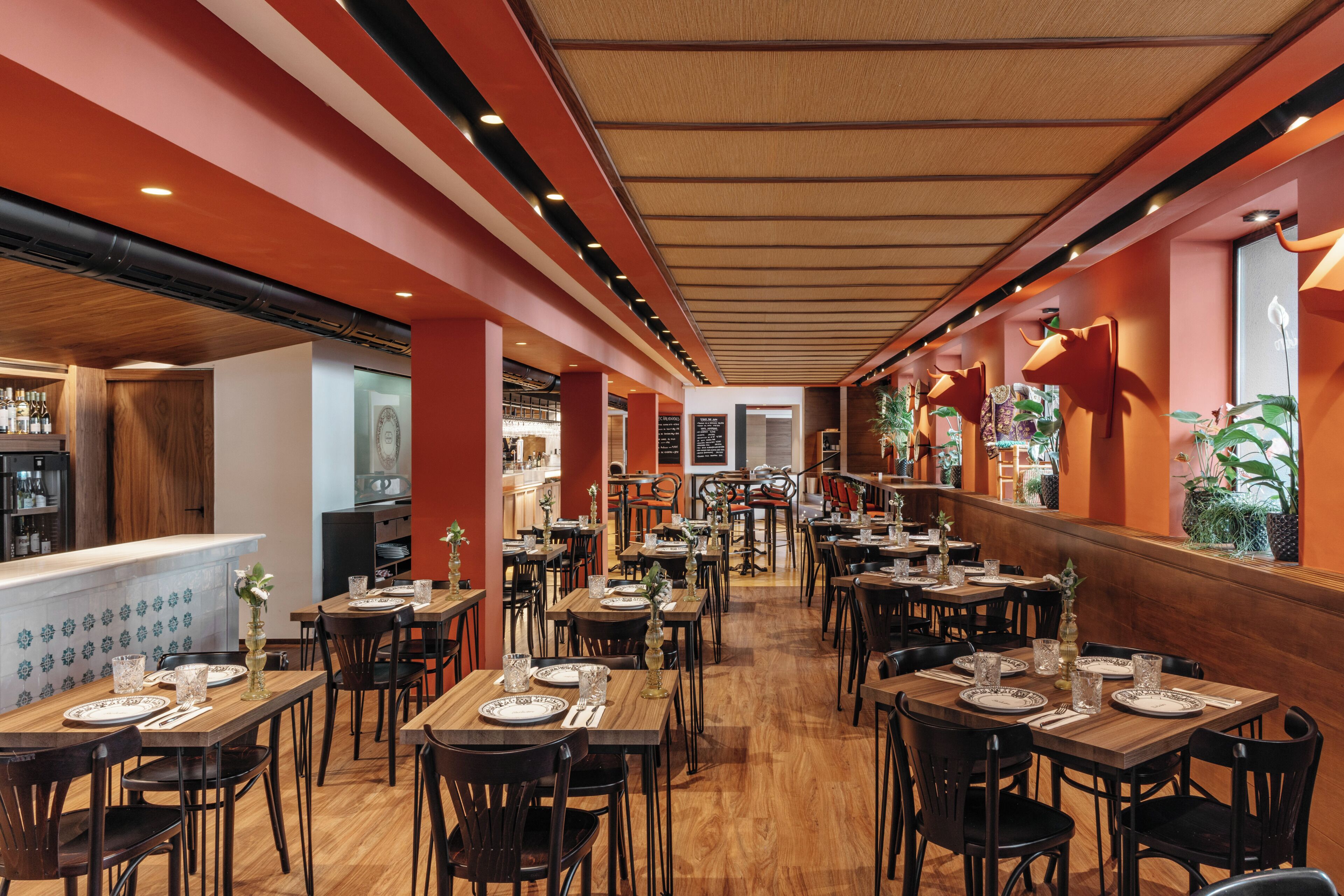 Un restaurante con mesas y sillas de madera, una zona de bar y vistas a la calle.