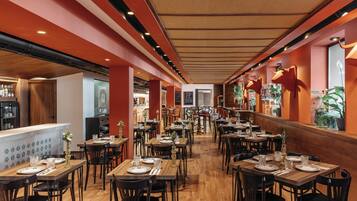 Un restaurante con mesas y sillas de madera, una zona de bar y vistas a la calle.