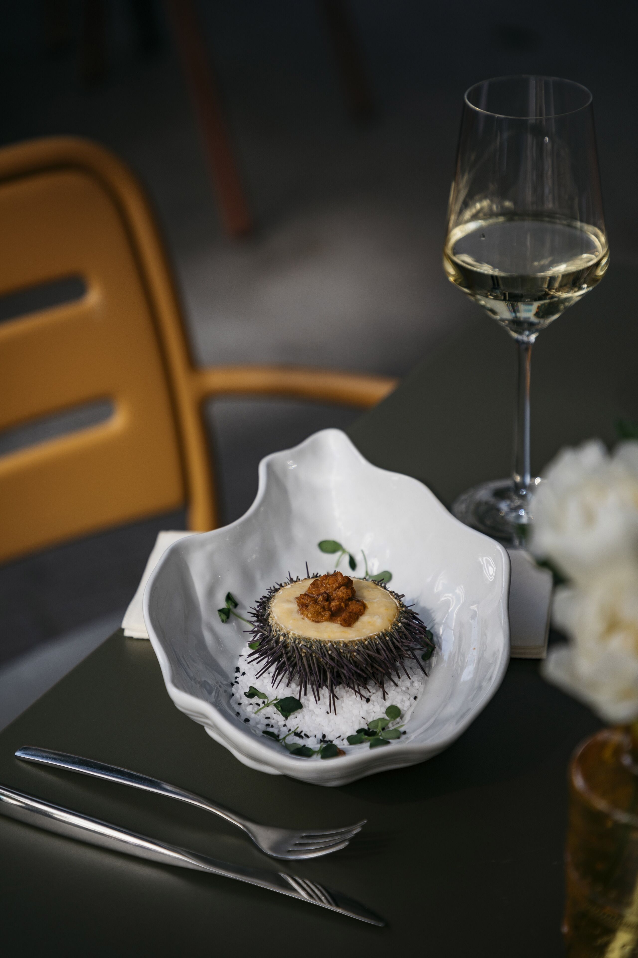 A dining table with a white bowl containing a seafood dish, a wine glass, and cutlery.