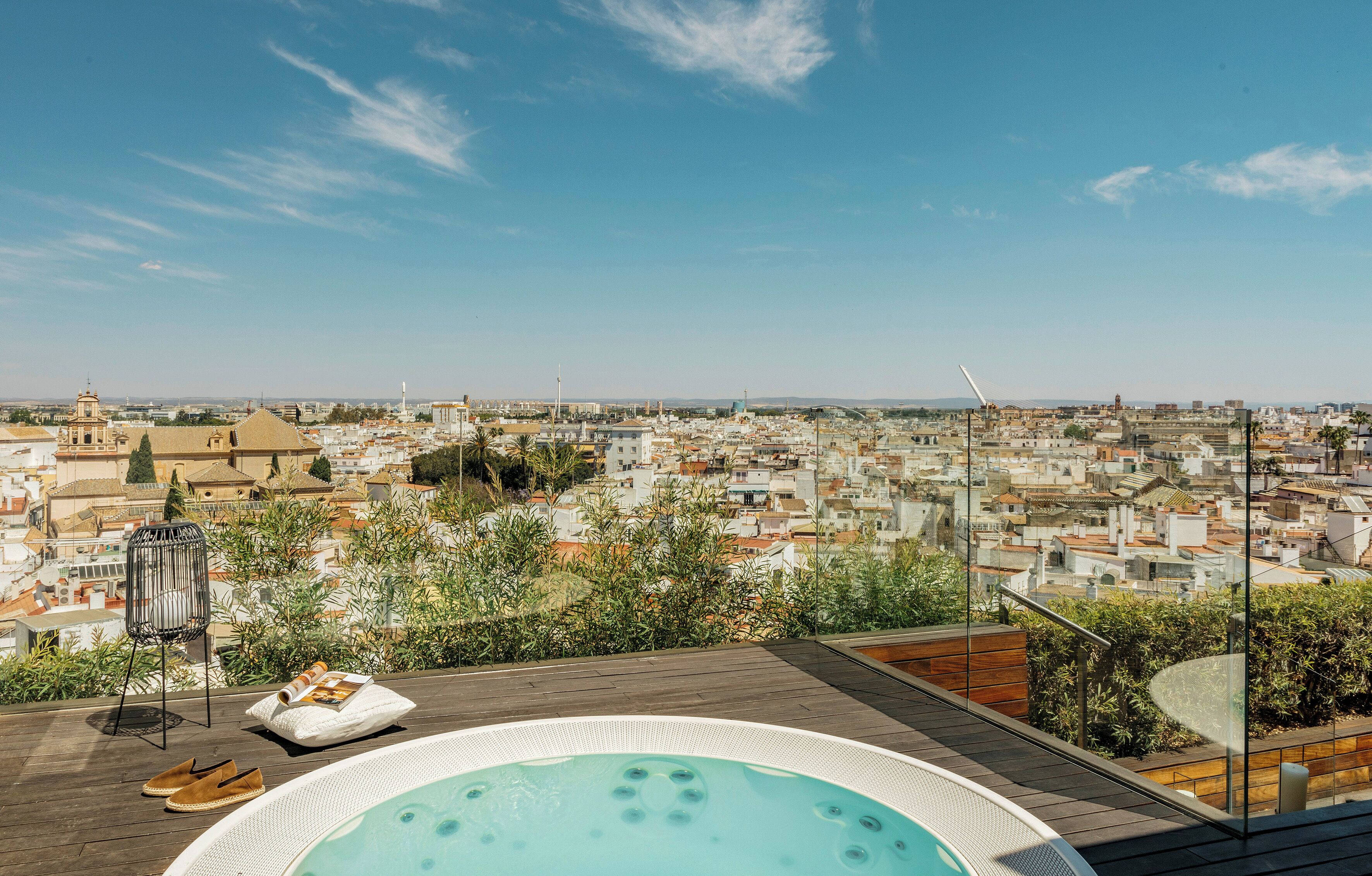 A rooftop terrace with a hot tub, lounge chairs, and a view of a cityscape.