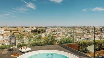 A rooftop terrace with a hot tub, lounge chairs, and a view of a cityscape.