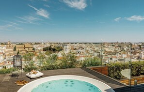 A rooftop terrace with a hot tub, lounge chairs, and a view of a cityscape.