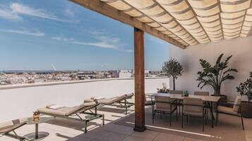 A rooftop terrace with lounge chairs, a dining table, and potted plants.