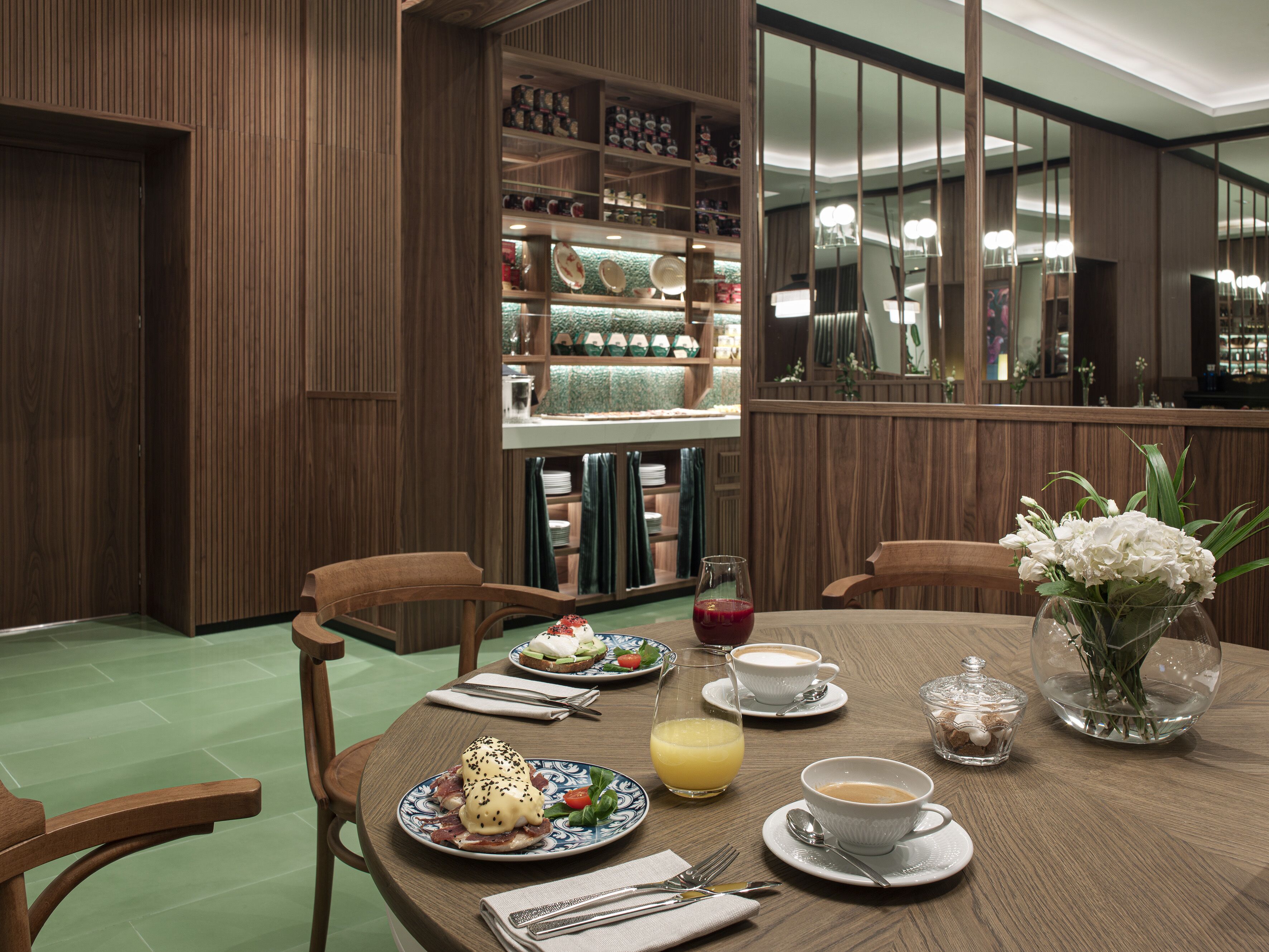 Un comedor con muebles de madera, una mesa dispuesta con platos, tazas y un jarrón de flores.