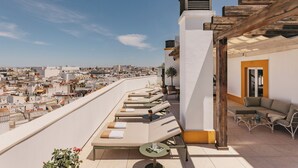 A rooftop lounge with sun loungers, a small table, and a view of the cityscape.
