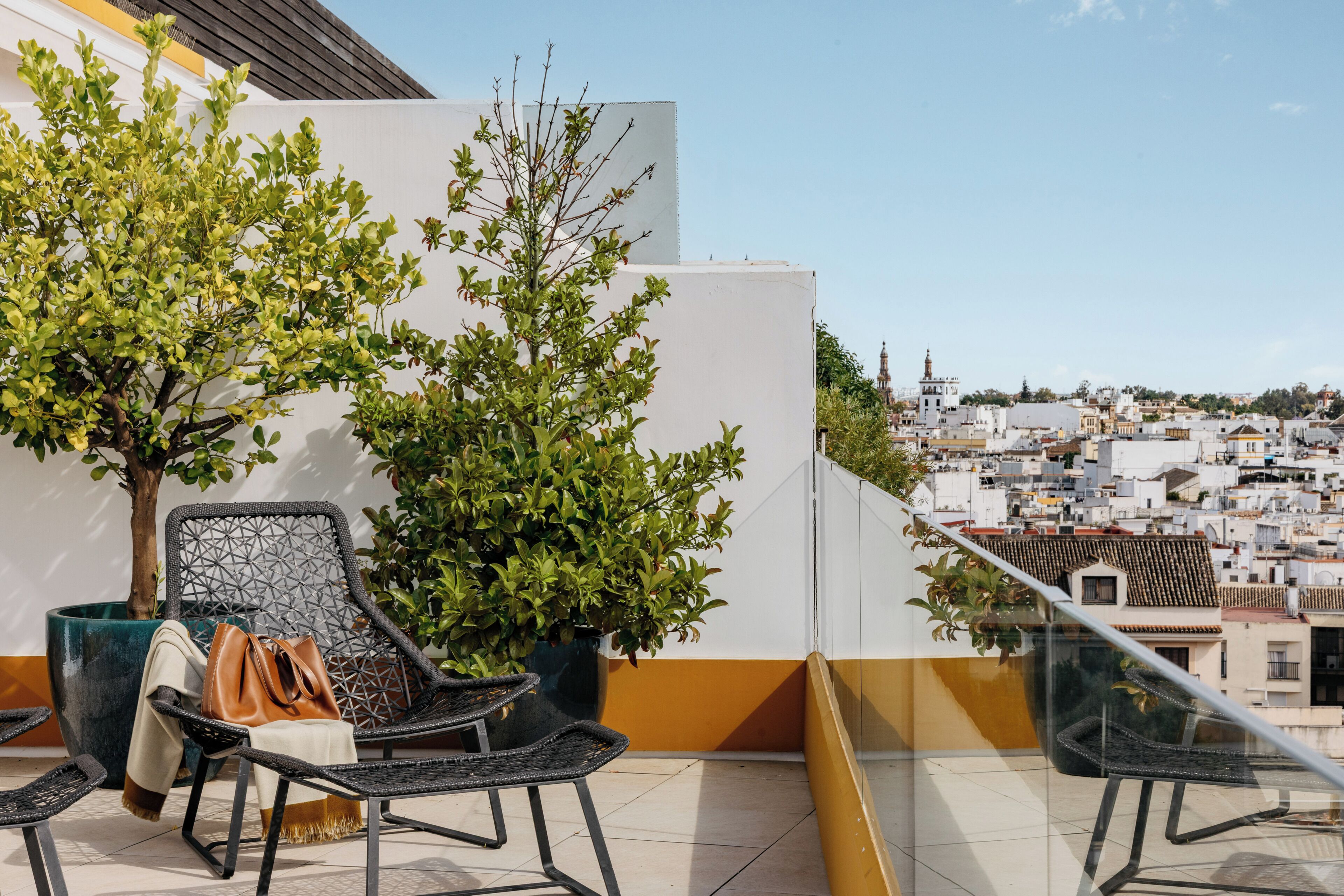 A balcony with two wicker chairs, a potted plant, and a view of a cityscape.