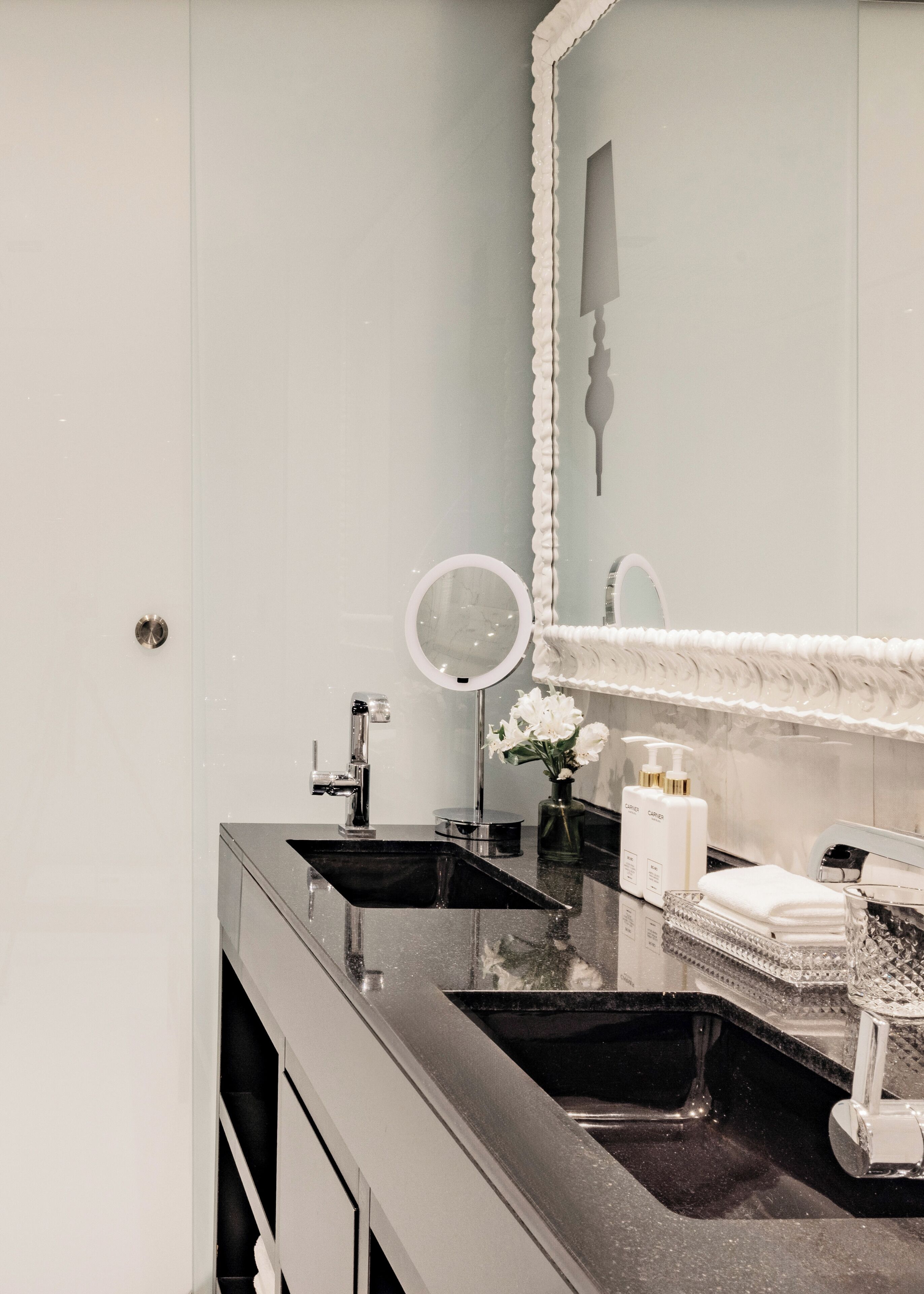 A bathroom with a double sink, a round mirror, and a vanity with a mirror.