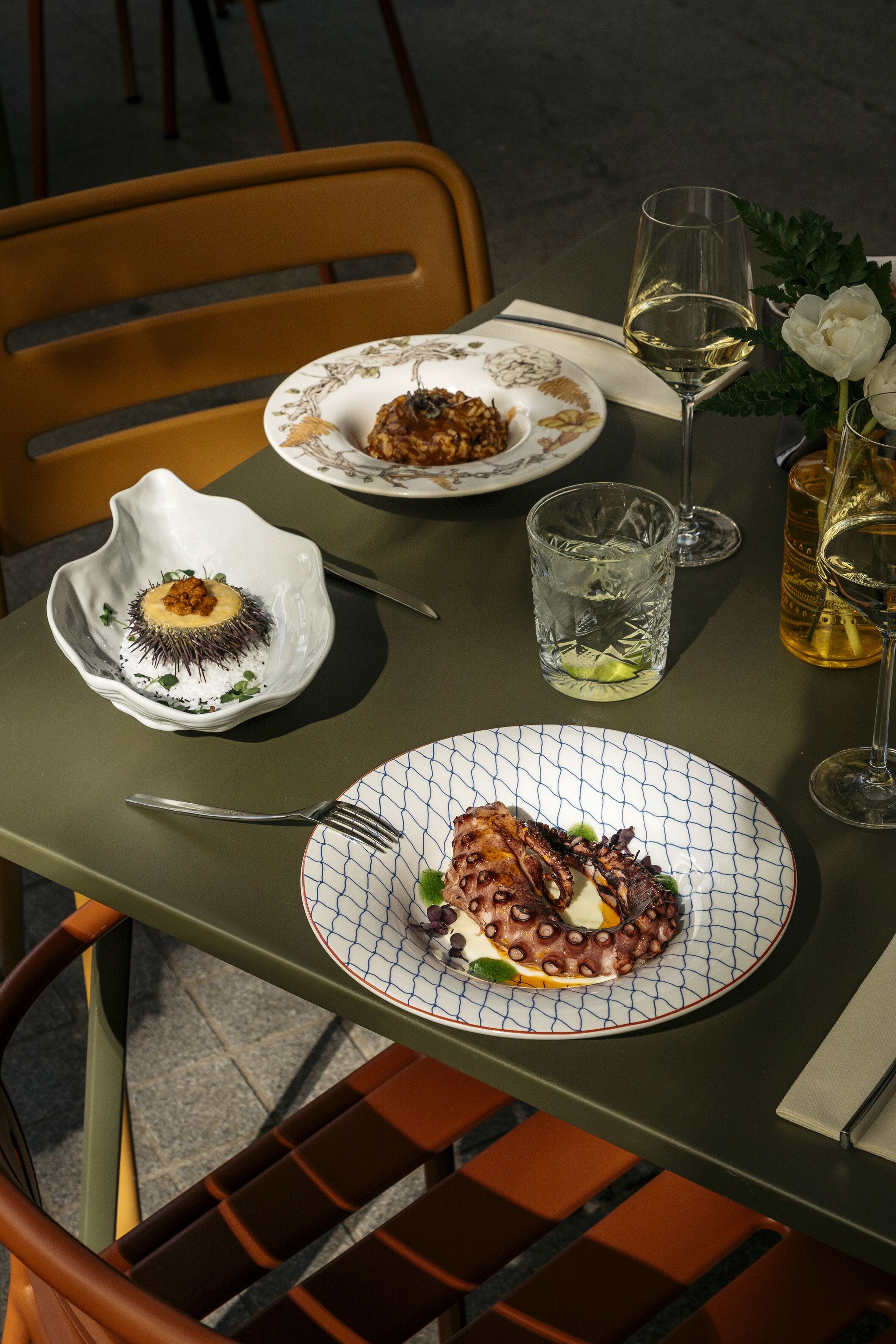 A table set with plates of food, glasses of wine, and a vase with flowers.