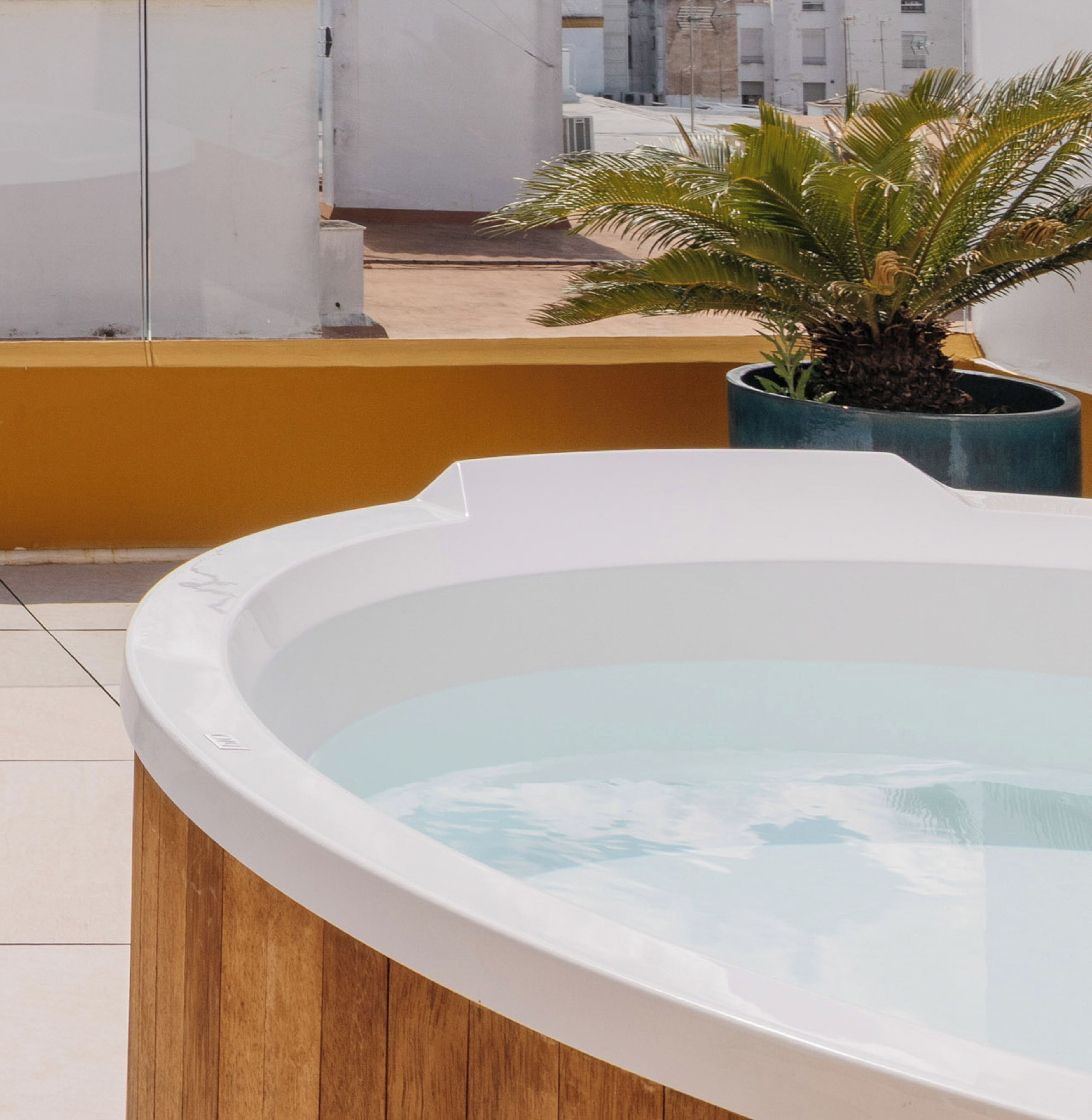 A hot tub on a balcony with a view of a building and a palm tree.