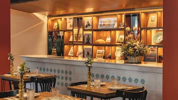 Een restaurantinterieur met houten tafels, stoelen, een betegelde spatwand, en een presentatie van ingelijste foto's en decoratieve objecten.