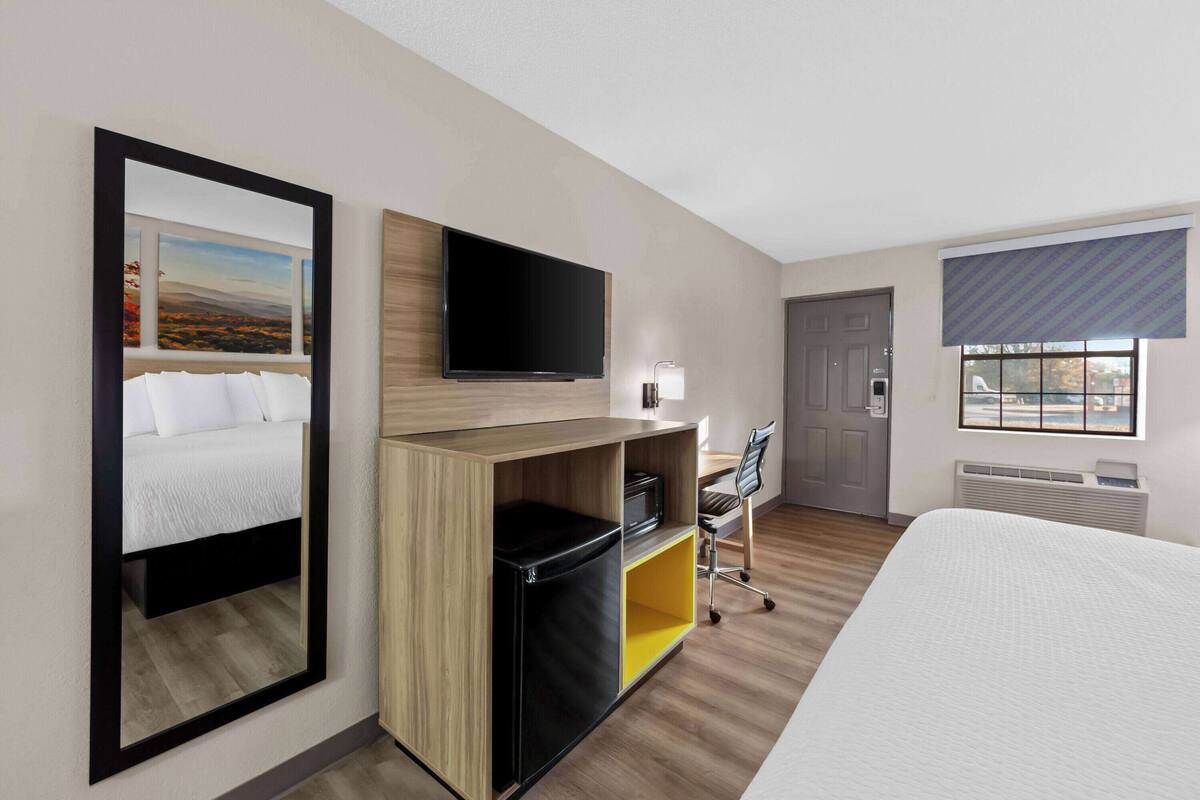 Une chambre d’hôtel comprenant un lit, un bureau avec une chaise, une télévision et une grande fenêtre donnant sur un beau paysage.