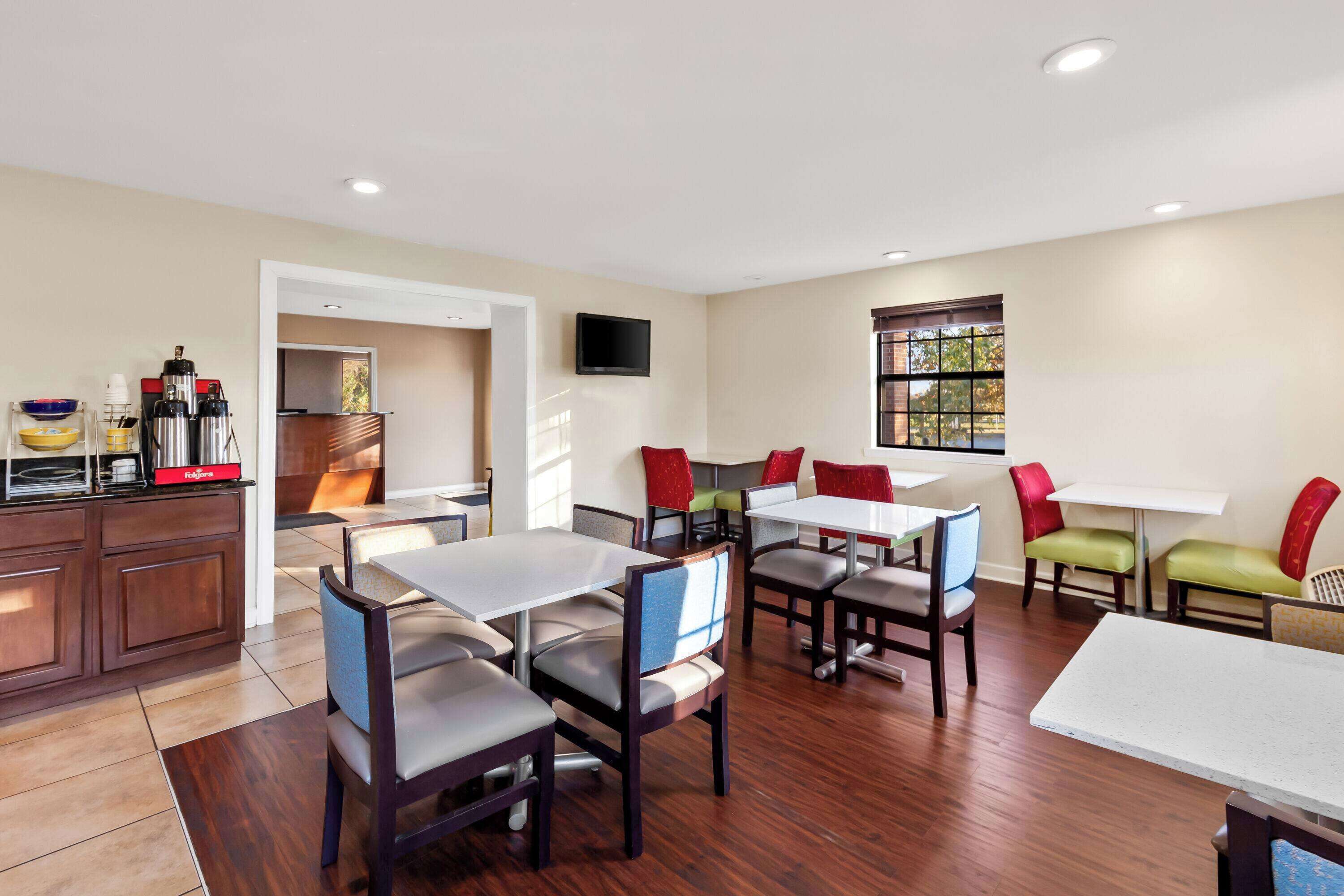 A modern dining area with multiple tables and chairs, a kitchen area with appliances, and a television mounted on the wall.