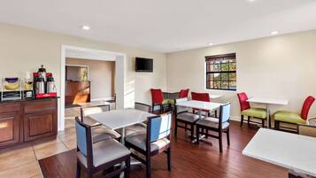 A modern dining area with multiple tables and chairs, a kitchen area with appliances, and a television mounted on the wall.