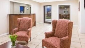 A hotel room with two patterned armchairs, a small table with a plant, and a reception desk.