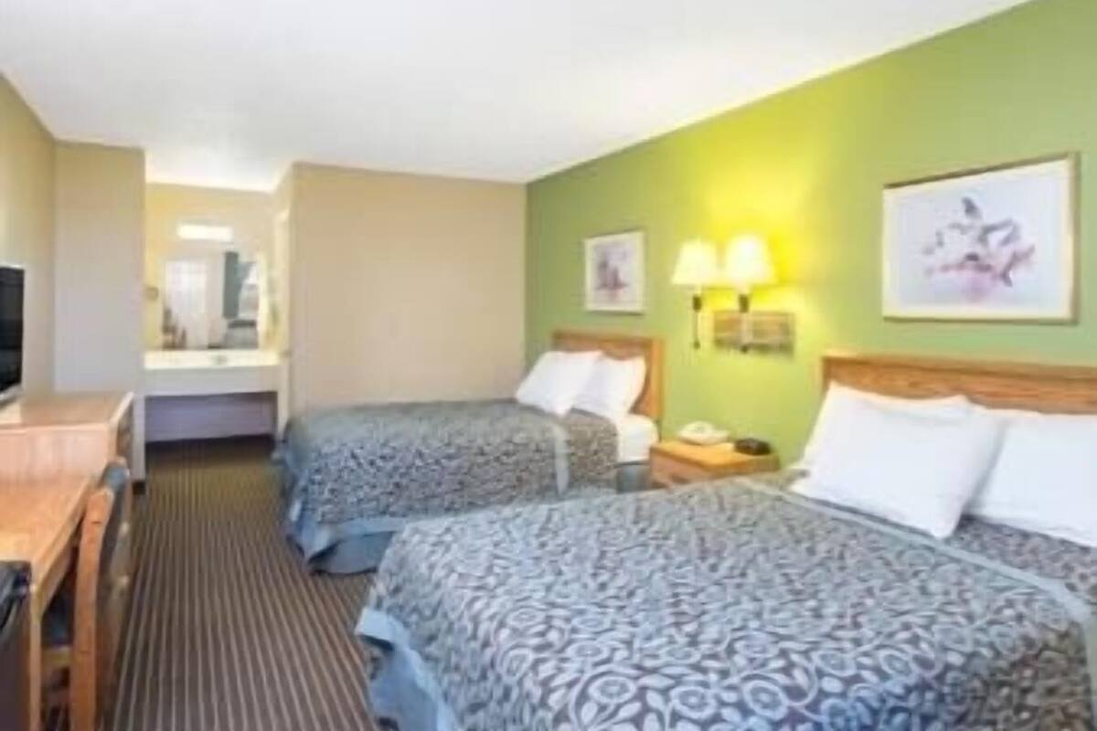 Une chambre d’hôtel avec deux lits, un bureau, une télévision et une salle de bain visible à travers une porte ouverte.