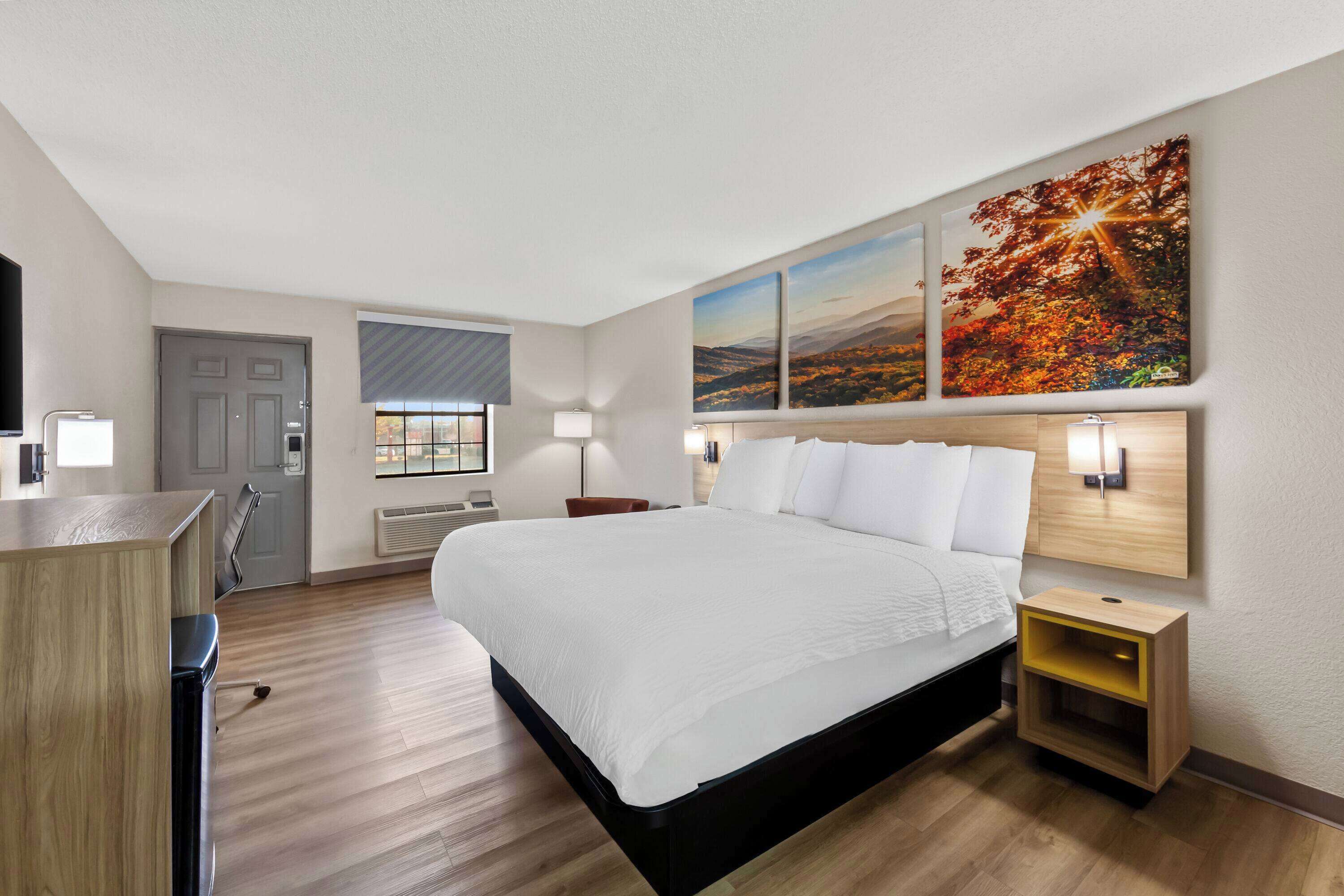 A modern hotel room with a large bed, a desk, and a window with blinds.