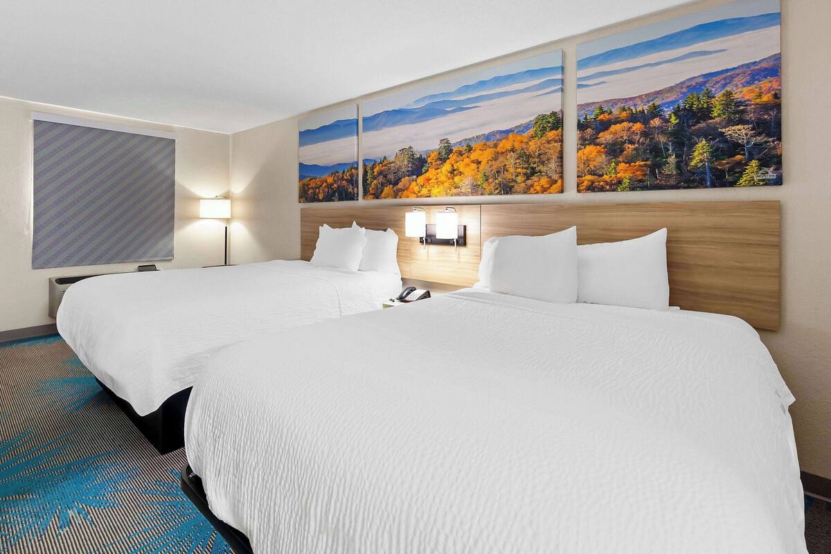 Une chambre d’hôtel avec deux lits, une grande fenêtre donnant sur le paysage automnal et une lampe fixée au mur.