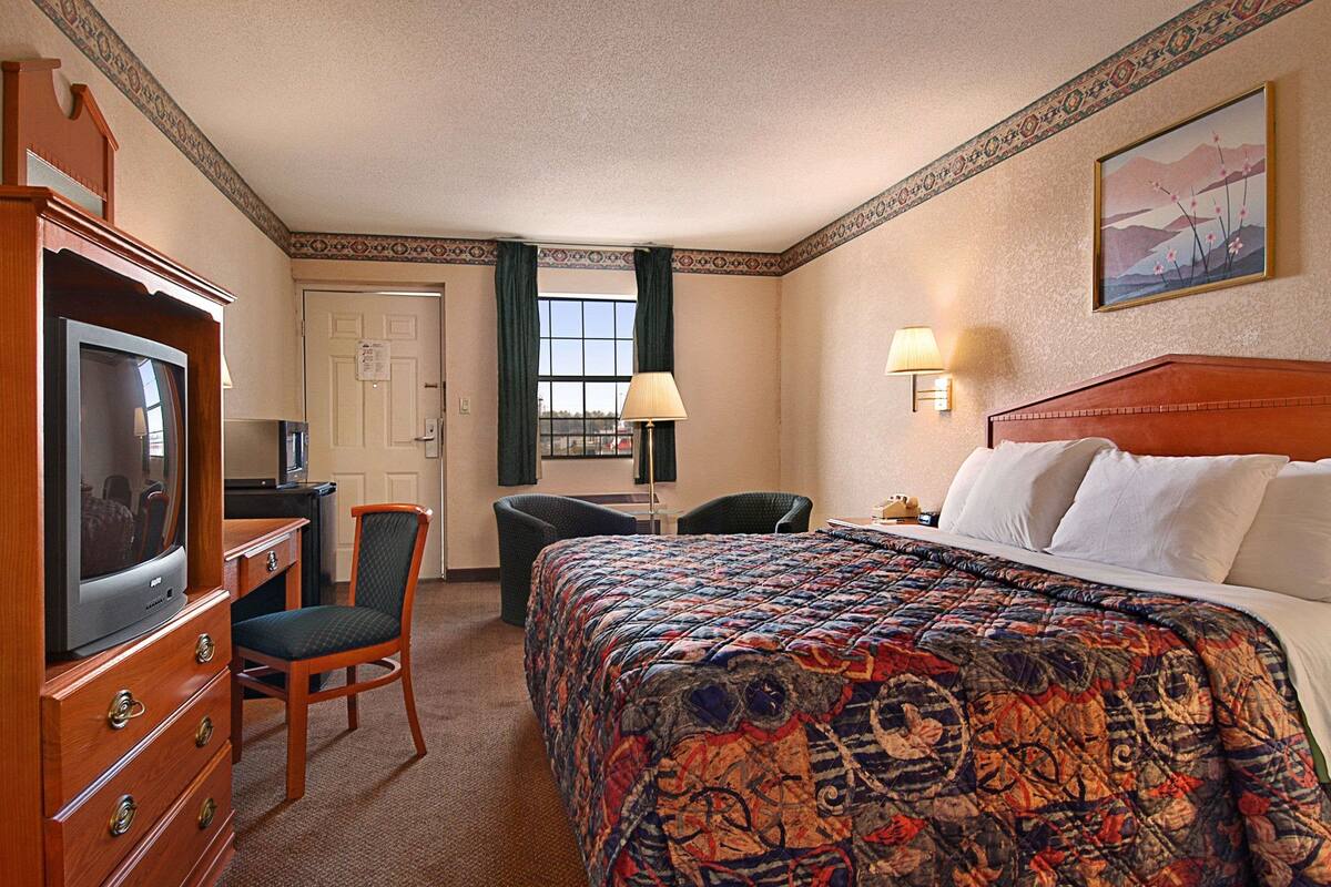Une chambre d’hôtel comprenant un lit, une télévision, un bureau avec une chaise, une lampe et un tableau au mur.
