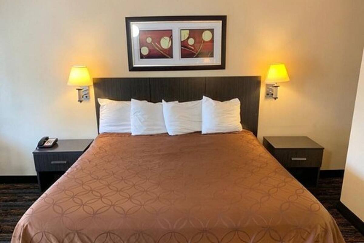 A hotel room with a large bed, two bedside tables, a framed picture above the bed, and two wall-mounted lamps.