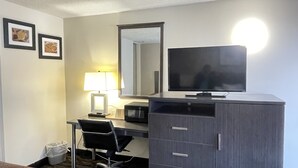 Habitación de hotel con escritorio, silla, televisor, lámpara, espejo y un cesto de basura.